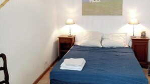 A bedroom with a bed, two bedside lamps, a painting of a house, a chair, and a hanging lamp. - Aigues-Mortaise house in the city (Aigues-Mortes)