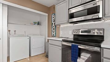 A kitchen with a built-in oven, microwave, and a hanging sign that reads 'BEACH'.