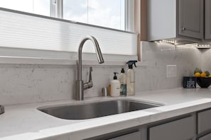 A modern kitchen with a stainless steel sink, a window above the sink, and a countertop with a bowl of lemons and a sign that reads "I NEED VITAMIN SEA."