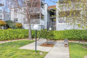A residential building with balconies, a well-maintained garden, and a paved pathway.