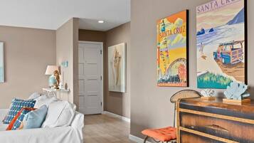 A room with a white sofa, a wooden dresser, and two wall-mounted artworks depicting Santa Cruz, California.