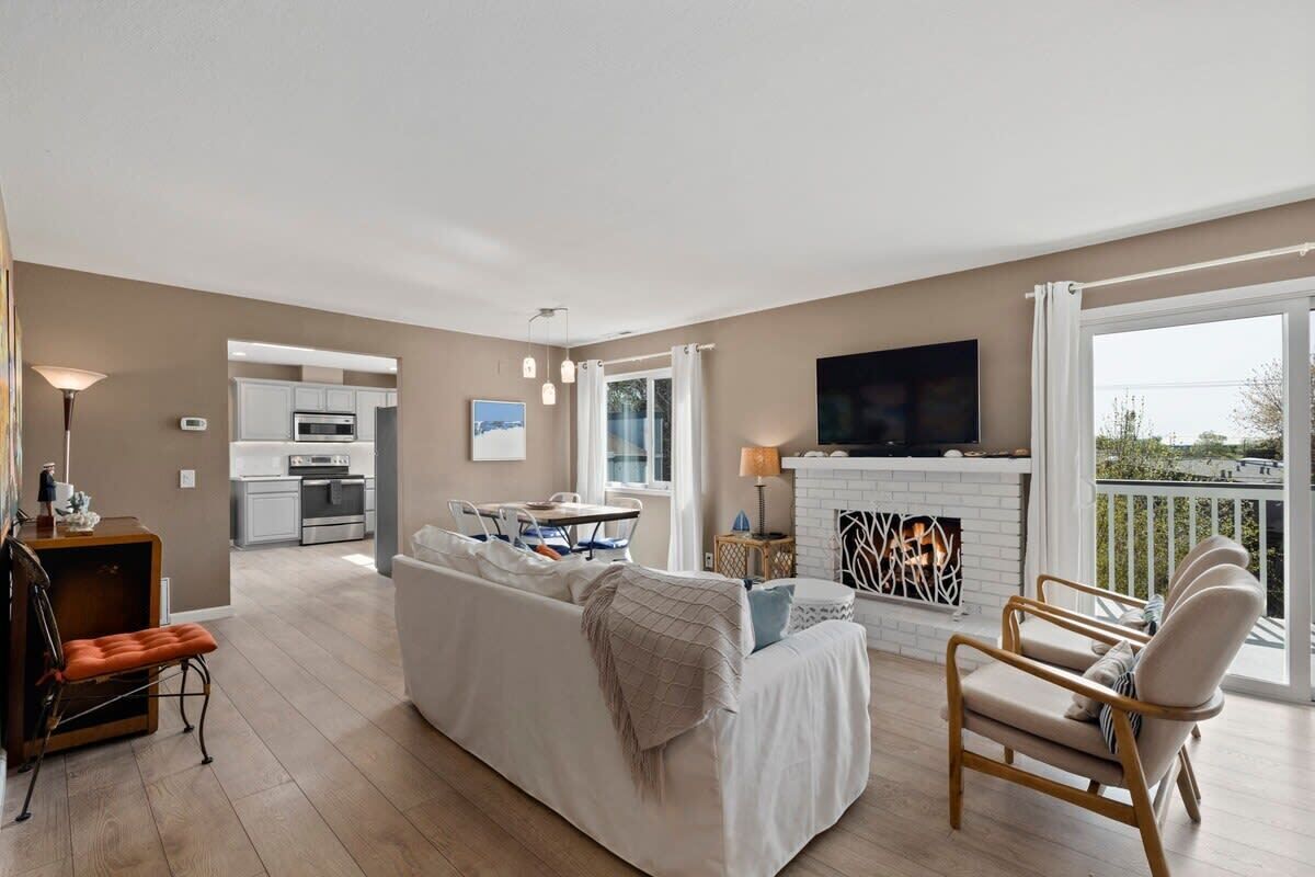 A modern living room with a sofa, armchairs, a fireplace, and a kitchen in the background.