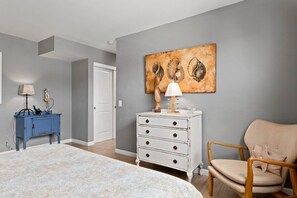 A bedroom with a bed, a dresser, a chair, and a wall-mounted lamp.