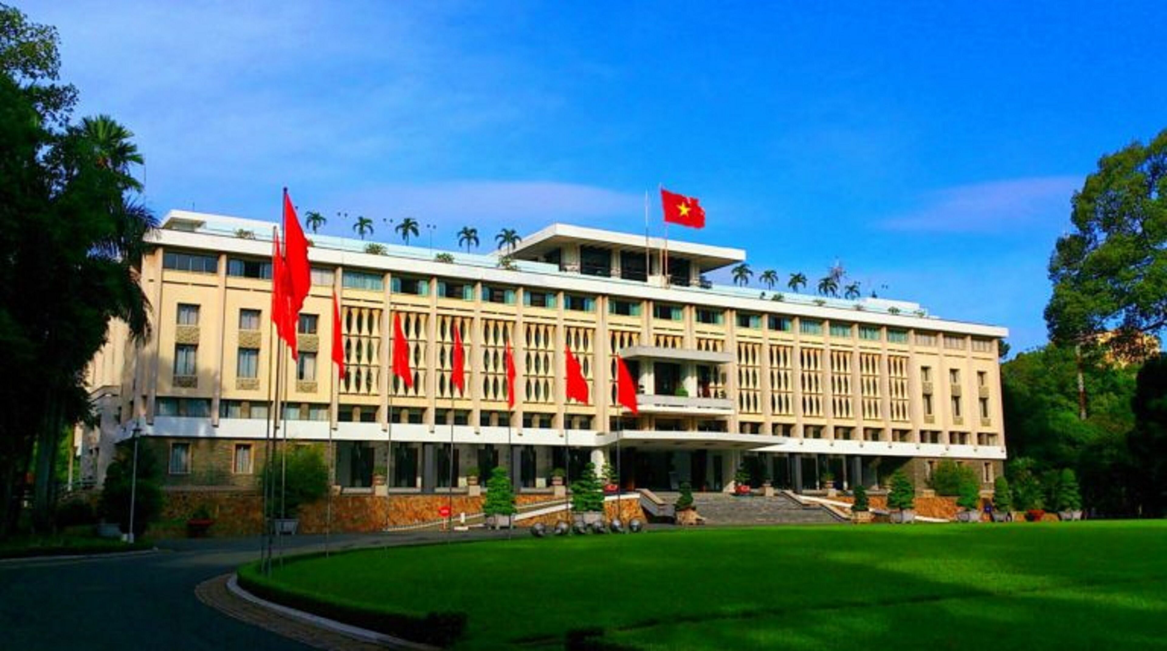 A large, multi-story building with a symmetrical facade, multiple red flags, and a flag on top.