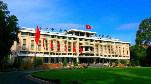 A large, multi-story building with a symmetrical facade, multiple red flags, and a flag on top.