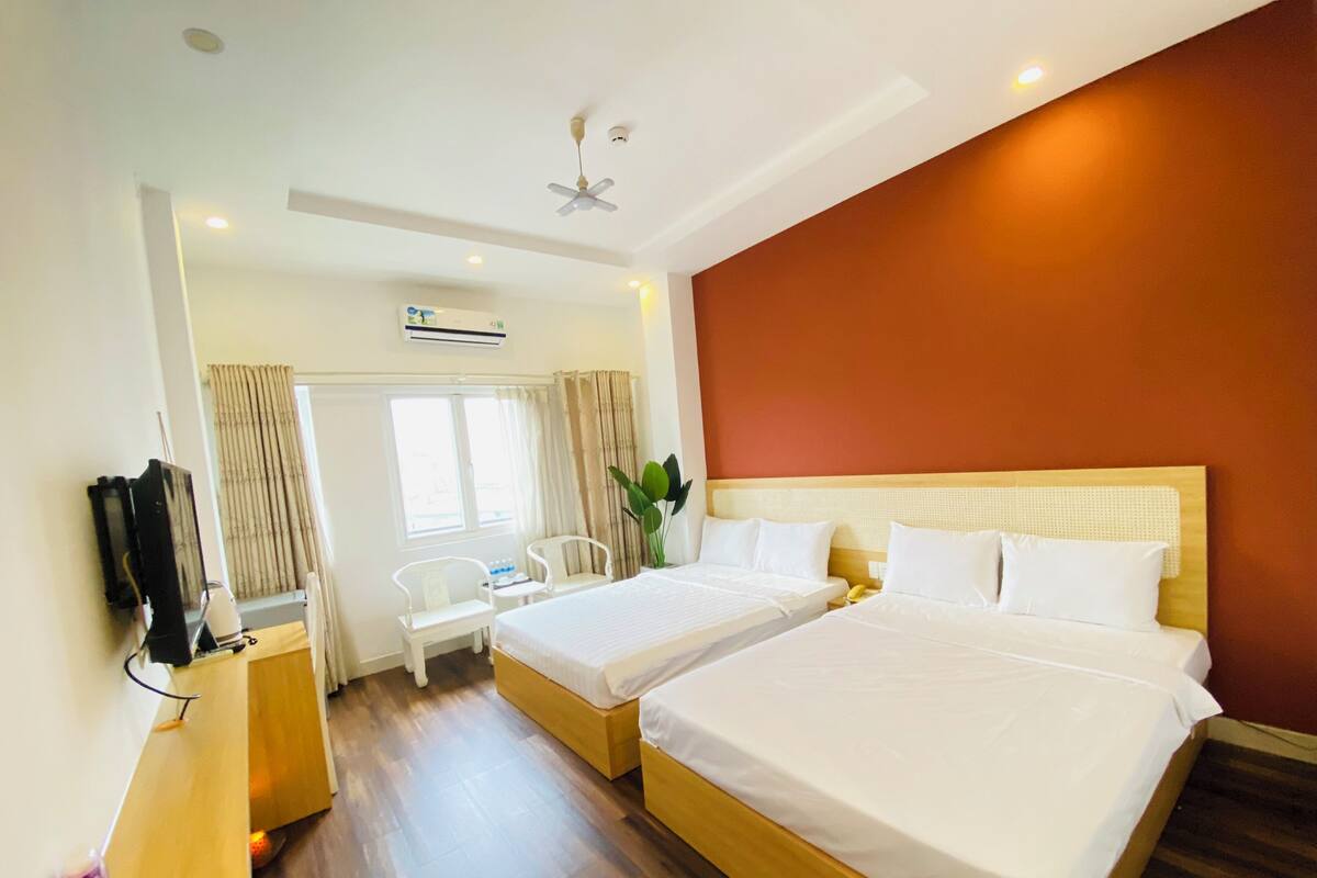 A hotel room with two beds, a TV, a desk, and a window with curtains.