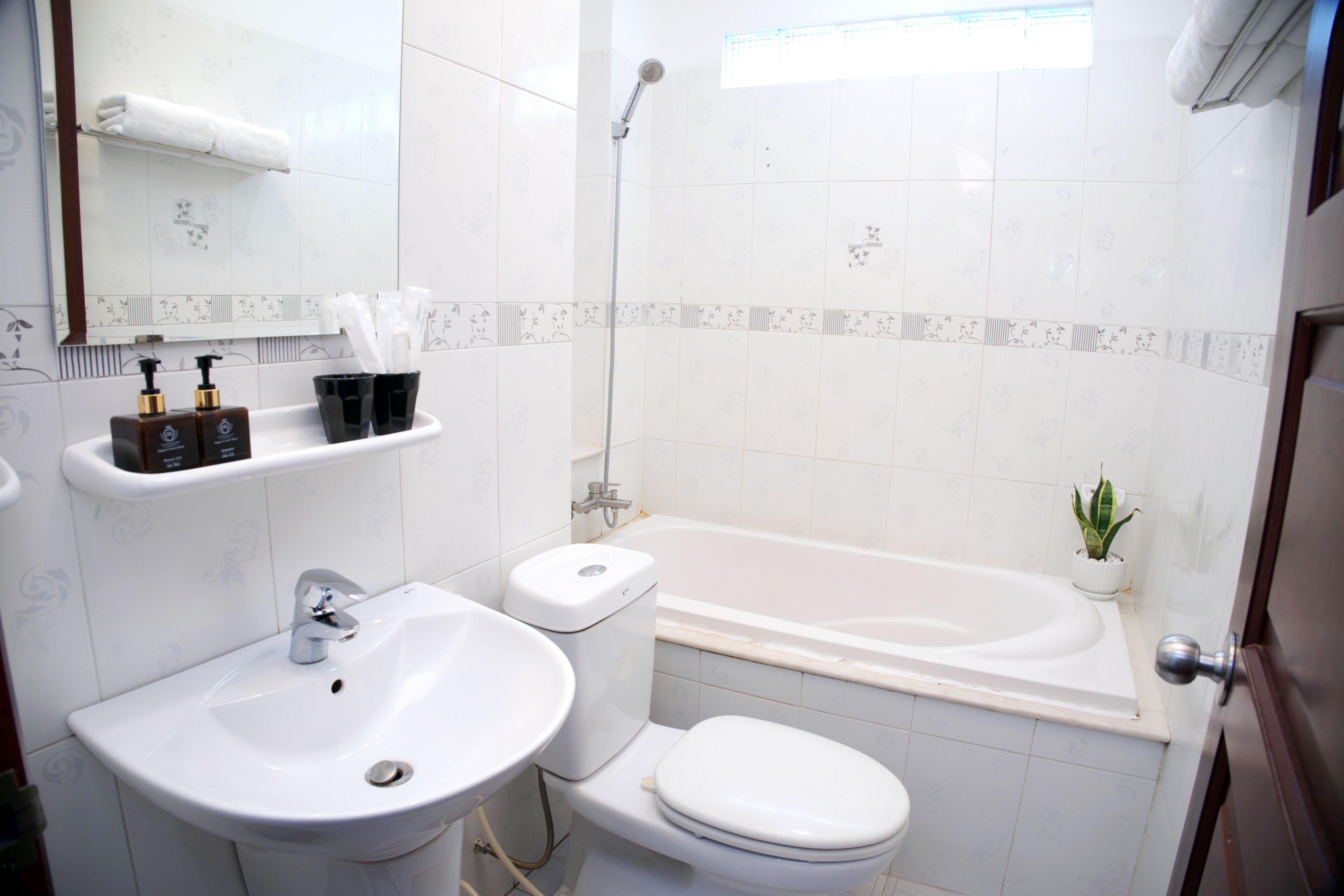 A bathroom with a sink, toilet, and bathtub. There is a towel rack above the sink and a small plant on the bathtub's edge.