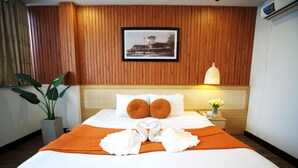 A hotel room with a wooden paneled wall, a framed picture, a bed with white linens, orange pillows, and a heart-shaped towel arrangement. - Saigon Central Hotel (Ho Chi Minh City)
