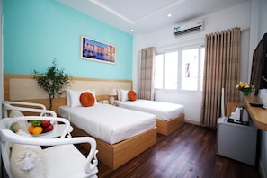 Quarto de hotel com duas camas, uma pequena mesa de trabalho, uma planta e uma janela com cortinas.