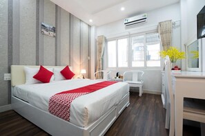 Quarto de hotel com uma cama, uma escrivaninha, uma cadeira, uma janela com cortinas e um aparelho de ar condicionado.