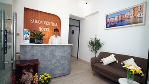 A reception desk with a sign reading "SAIGON CENTRAL HOTEL," a brown sofa with a vase of flowers, and a framed painting on the wall. - Saigon Central Hotel (Ho Chi Minh City)