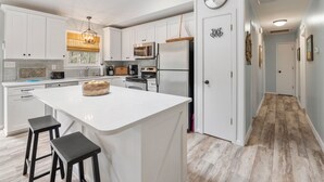 Cozinha moderna com armários brancos, uma ilha central com banquetas, eletrodomésticos de aço inoxidável e luminária pendente.
