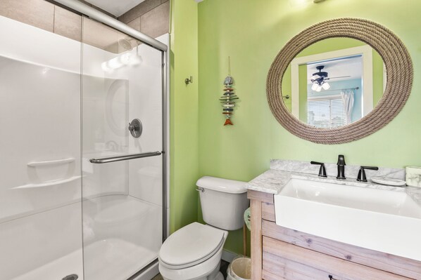 A bathroom with a glass-enclosed shower, a white toilet, and a vanity with a marble countertop. - Sea-Eye-Eh?: Oceanfront | Beach and Pool Access (Kill Devil Hills)