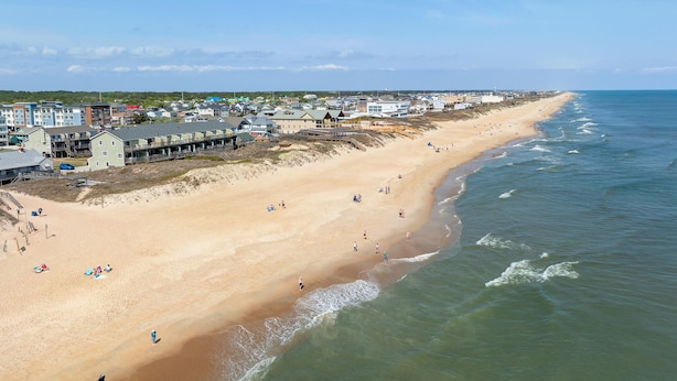 Une plage côtière bordée d’une rangée de bâtiments, dont certains sont dotés de balcons.