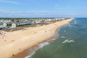 A coastal beach with a row of buildings along the shore, some with balconies. - Sea-Eye-Eh?: Oceanfront | Beach and Pool Access (Kill Devil Hills)