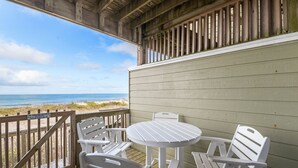 Une terrasse en bois avec des meubles d’extérieur blancs donnant sur une plage.