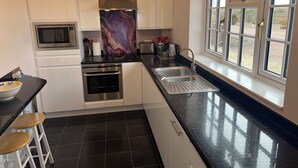 A modern kitchen with white cabinets, a stainless steel oven, a microwave, and a large window with a view of the outdoors. - The Lodge, South Cotswolds, contemporary rural home, Spa Pool, views, parking (Chippenham)