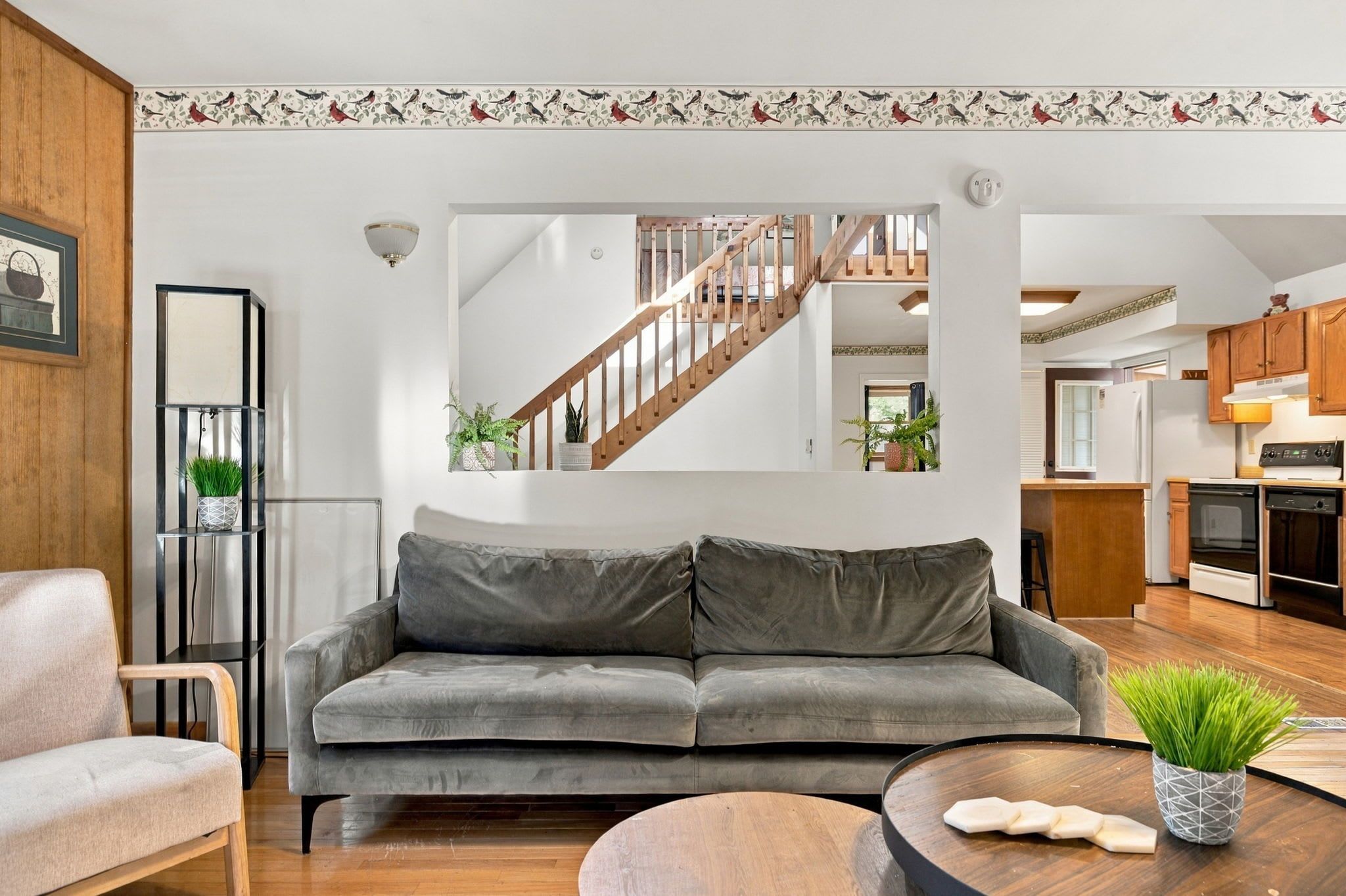 A modern living room with a grey sofa, wooden floor, and a staircase leading to an upper level.