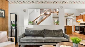 A modern living room with a grey sofa, wooden floor, and a staircase leading to an upper level.