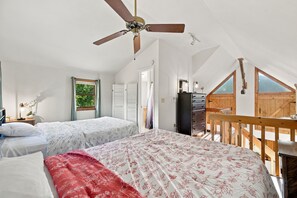 A bedroom with two beds, a ceiling fan, a wooden desk, a dresser, and a large window. - Group-friendly cabin w/ hot tub & deck (Great Cacapon)