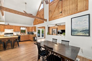 A spacious kitchen with wooden cabinets, a dining area with a large table and chairs, and a view of the outdoors. - Group-friendly cabin w/ hot tub & deck (Great Cacapon)