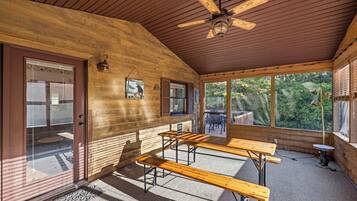A wooden cabin interior with a ceiling fan, wooden benches, and a view of the outdoors.