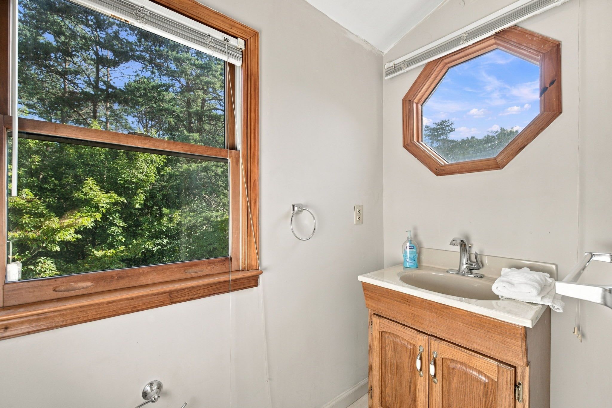 A bathroom with a wooden vanity, a sink, a mirror, and a window with a view of trees.