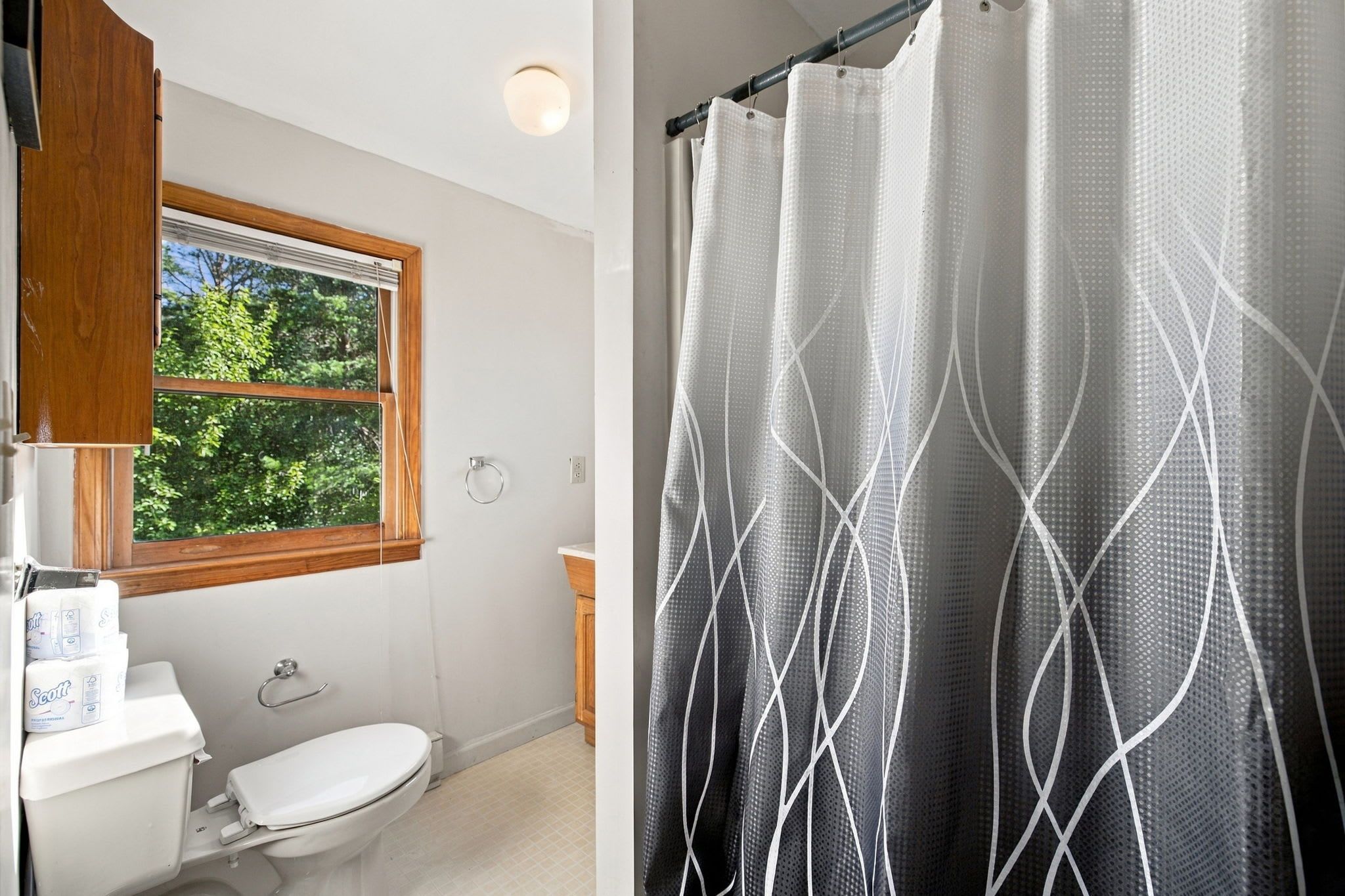 A bathroom with a toilet, a sink, a window, and a shower curtain with a geometric pattern.