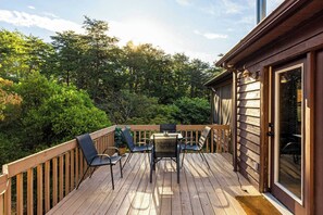 A wooden deck with a table and chairs, surrounded by a railing, overlooking a forested area. - Group-friendly cabin w/ hot tub & deck (Great Cacapon)