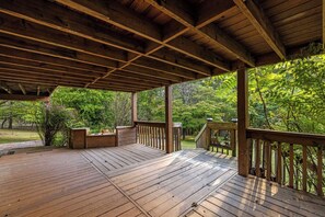 A wooden deck with a covered area, surrounded by lush greenery.