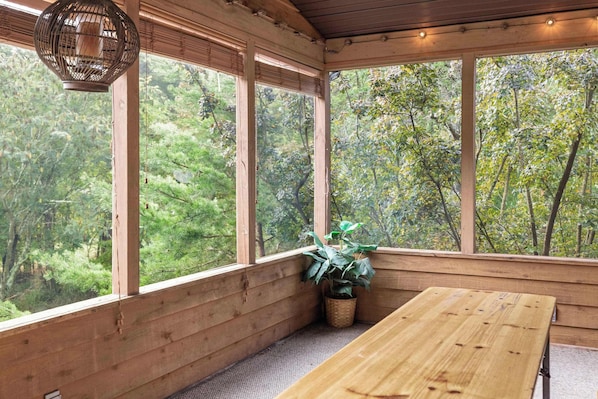 Interior de madeira com grandes janelas, uma mesa de madeira e um candeeiro pendente.