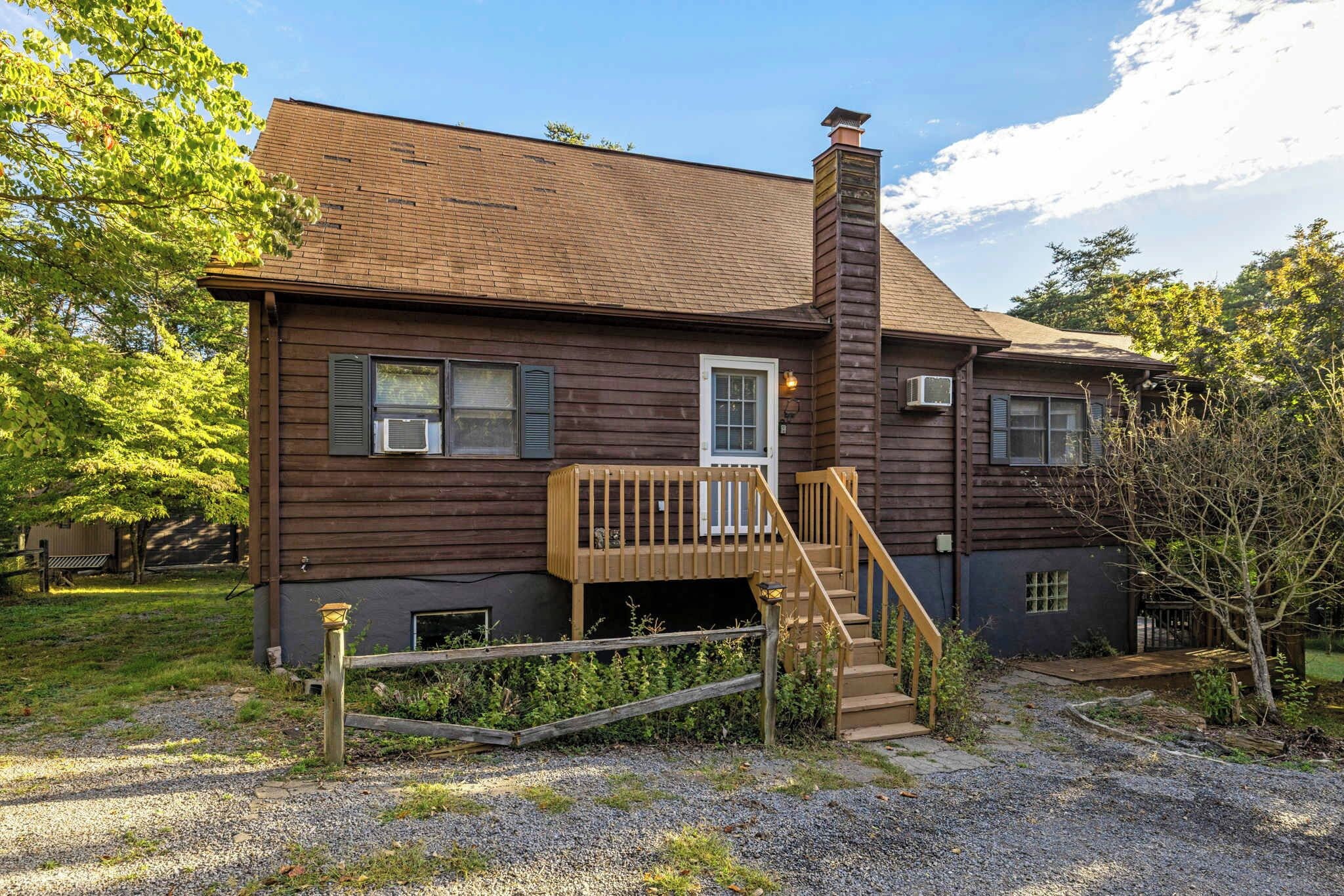 Une maison en bois à deux étages, dotée d’un porche à l’avant, d’une cheminée et d’une allée gravillonnée.
