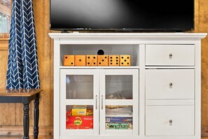 A white entertainment unit with a flat-screen TV, dice, and storage drawers.