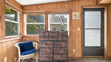 A room with wooden walls, a wicker chair, a wooden cabinet with drawers, and a door with frosted glass panels.
