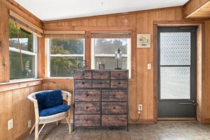 Ein Zimmer mit Holzwänden, einem Korbsessel, einem Schrank mit Schubladen und einer Tür mit satinierten Glaseinsätzen.