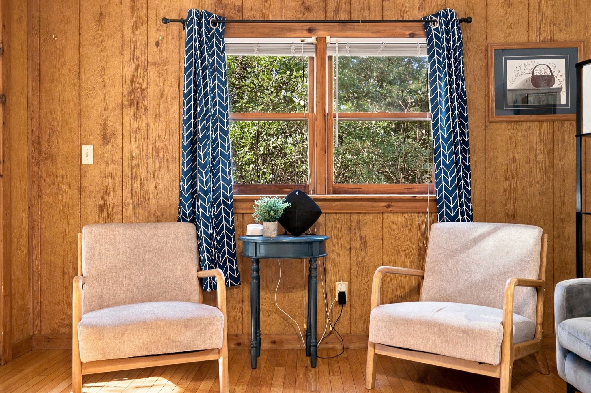 A room with two armchairs, a small table with a plant, and a window with curtains.