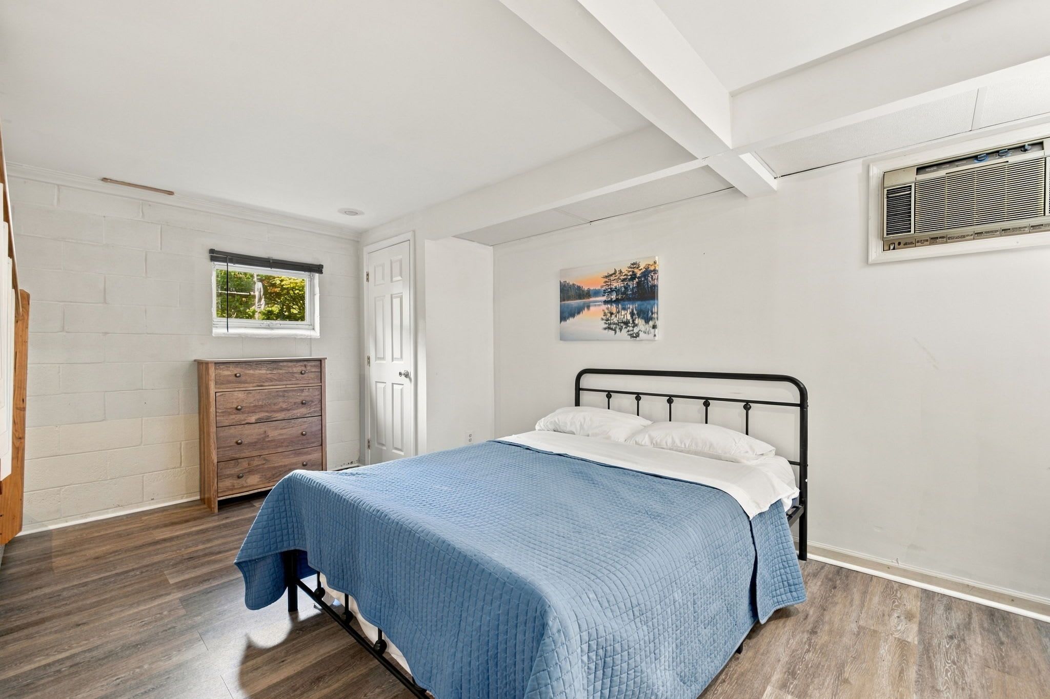 Une chambre à coucher avec un lit, une commode, une fenêtre et un tableau au mur.