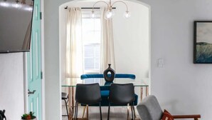 Un coin repas avec une table en verre, deux chaises noires, un canapé bleu et un lustre moderne.