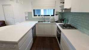 A modern kitchen with a central island, a built-in dishwasher, a stove, and a window with a view of the city. - A Cozy room in Center of Glen (Glen Waverley)