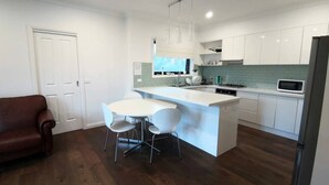 A modern kitchen with white cabinets, a central island, and a dining area with two chairs. - A Cozy room in Center of Glen (Glen Waverley)