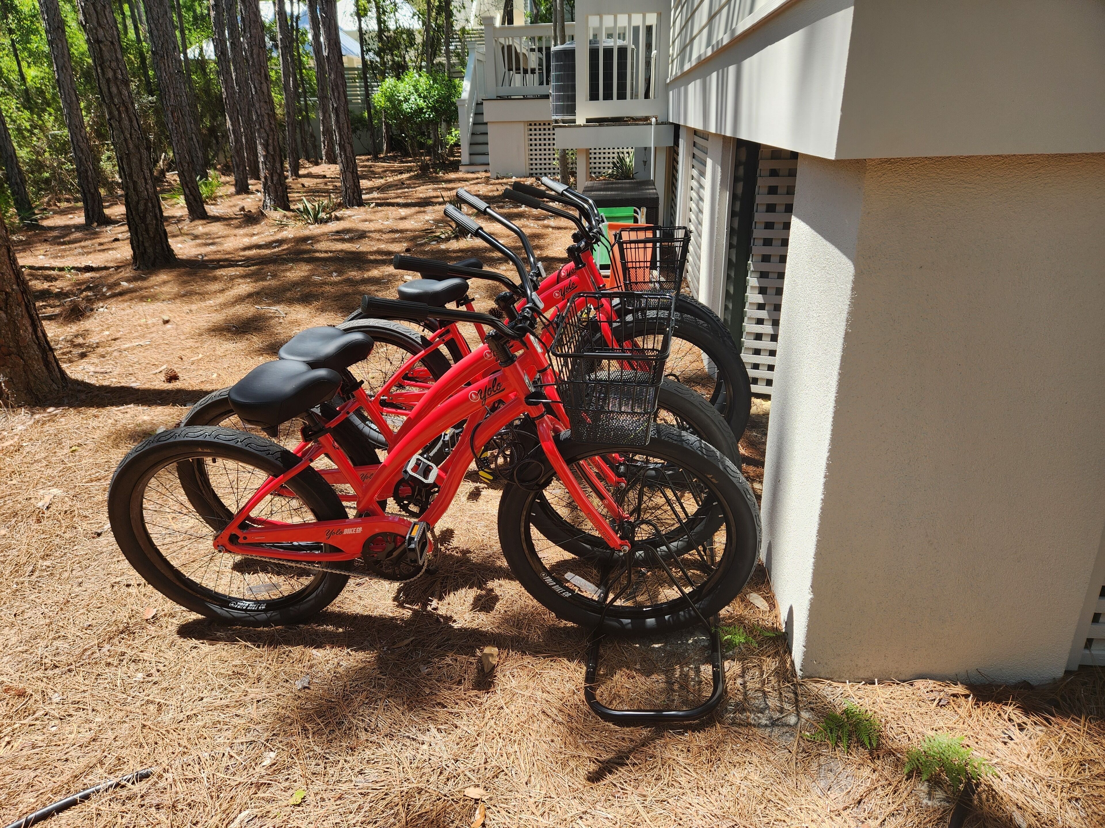 A row of red bicycles parked outdoors with a building in the background.