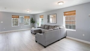 A spacious living room with a grey sectional sofa, two windows with blinds, and a ceiling light fixture. - Gorgeous Waterfront 2:1 - 2 houses in 1 building. (New Haven)