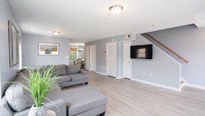 A modern living room with a grey sectional sofa, a small table with a plant, and a staircase with a wooden handrail. - Gorgeous Waterfront 2:1 - 2 houses in 1 building. (New Haven)