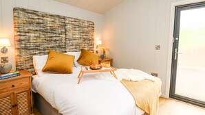 Un dormitorio con cama, almohadas, mesitas de noche, lámpara y ventana.