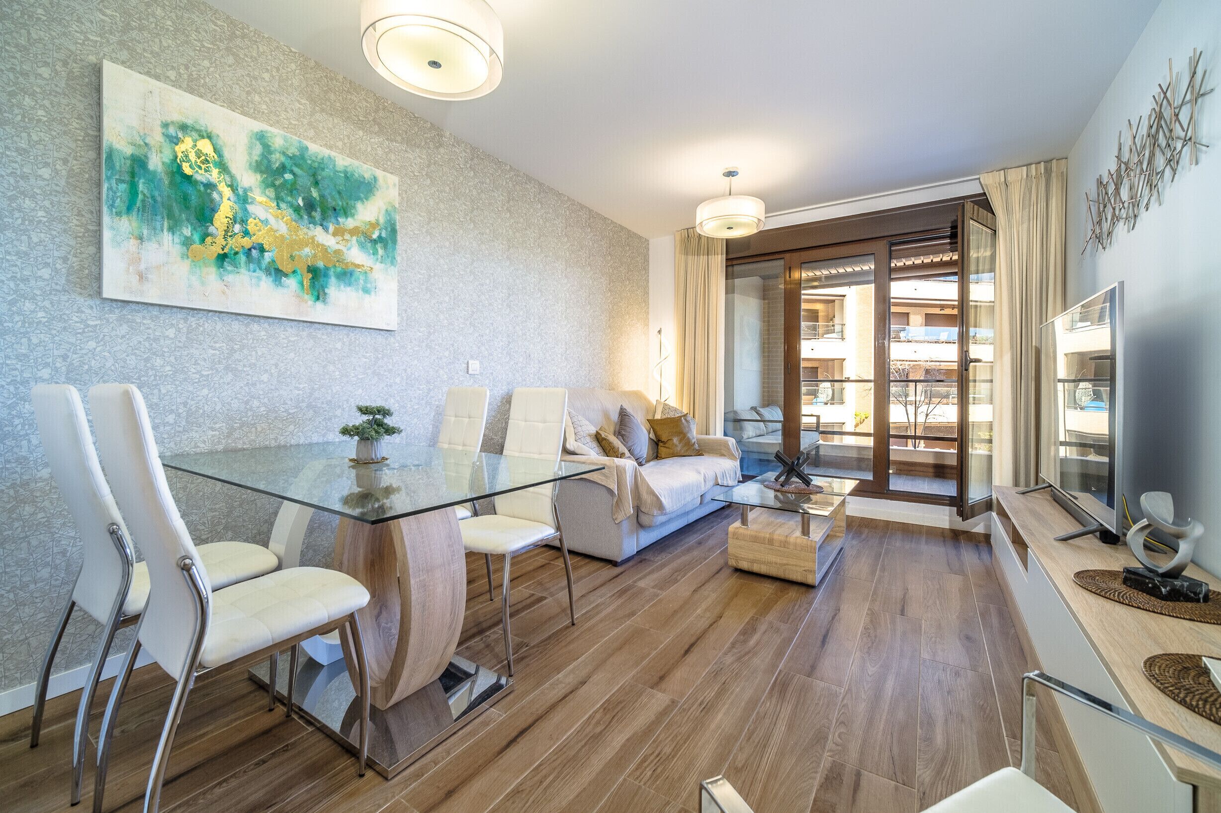 A modern living room with a glass dining table, a sofa, and a large abstract painting on the wall.
