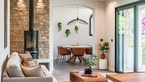 Een moderne woonkamer met een stenen muur, een open haard, een eethoek met stoelen en een groot raam.