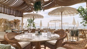 Een terras met rieten meubels, witte parasols en uitzicht op zee.