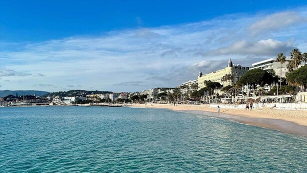 Een kustgezicht met helder turquoise water, een zandstrand en een opvallend wit gebouw met een koepel aan de rechterkant.