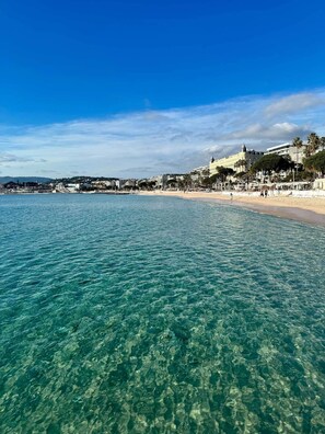 A coastal cityscape with clear turquoise waters, a sandy beach, and a prominent white building with a dome on the right. - Totolulu Cannes Luxury Properties - The Villa (Cannes)