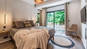 Een moderne slaapkamer met een groot bed, een zachte deken, een houten vloer, een rond tapijt, een hanglamp en uitzicht op de natuur door een schuifpui.
